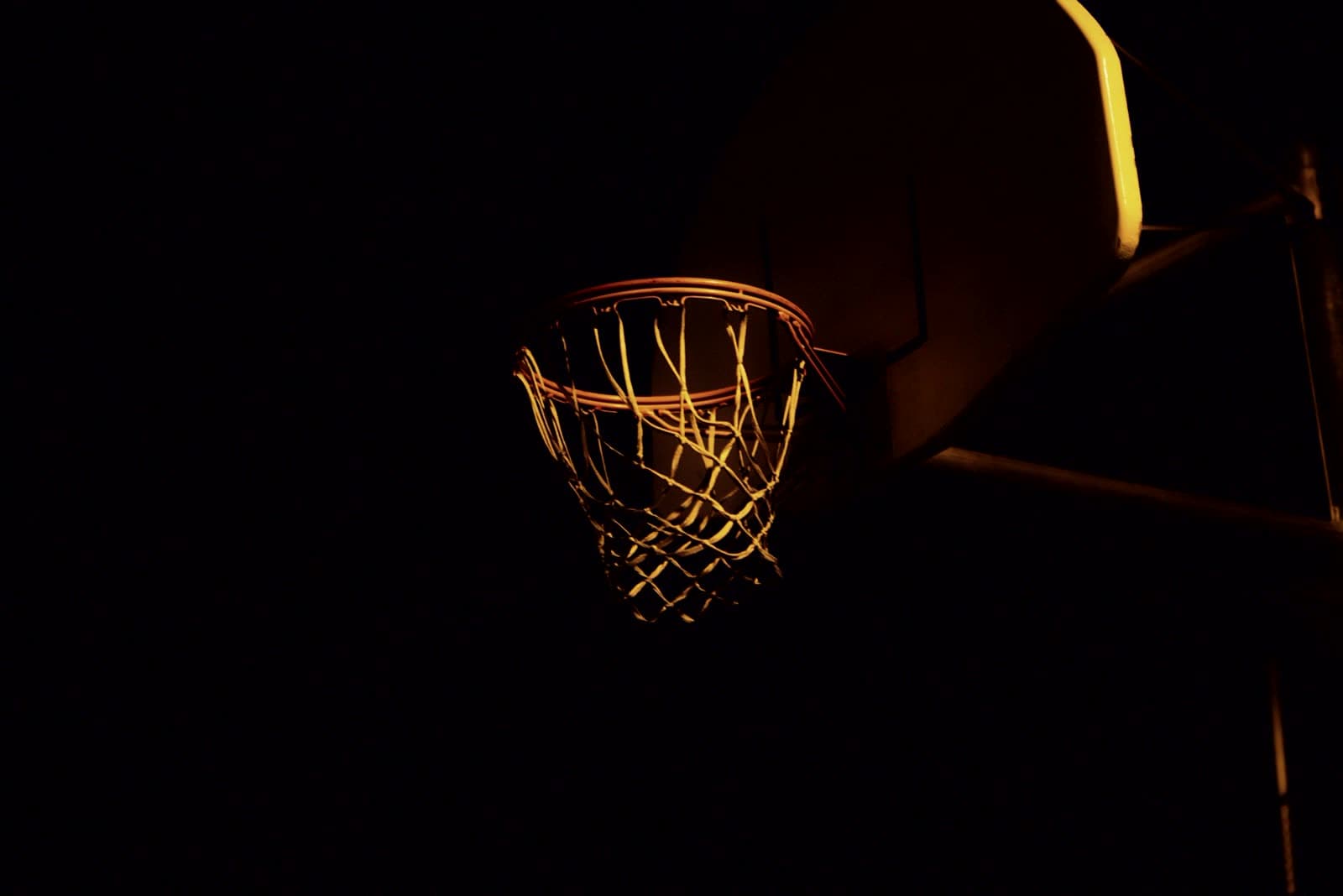 Basketball rim and net lit against a dark gym