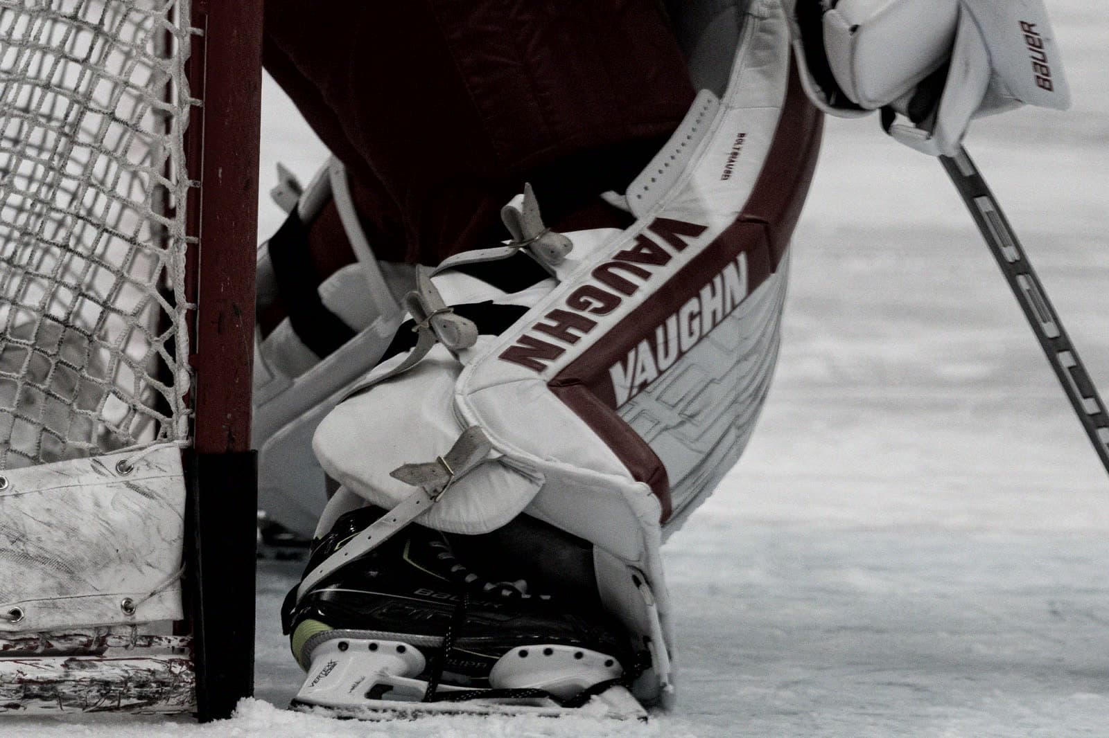 Goalie pads and skates beside the net, pucks on the ice